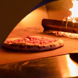 Pizza being cooked in Alfa Moderno 2 Pizze Wood Fired Pizza Oven in Antique Red with flames visible.