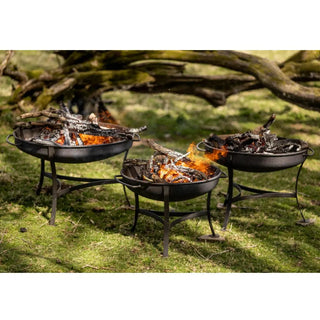 Three Dean Forge Moorland Firebowl outdoor fire pits with flames on a grassy area with trees in the background