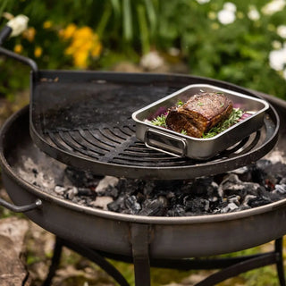 Grilled dish on a pan over charcoal on Dean Forge Moorland Firebowl and Swing Arm Set with a natural outdoor background