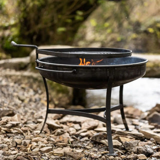 Dean Forge Moorland Firebowl and Swing Arm Set fire pit with flames on a rocky outdoor surface