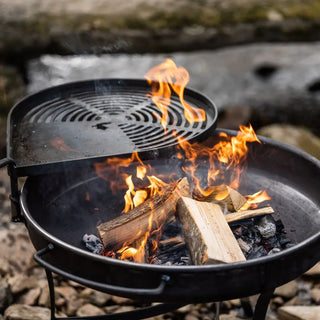 Dean Forge Moorland Firebowl and Swing Arm Set fire pit with flames and wooden logs on a natural stone background