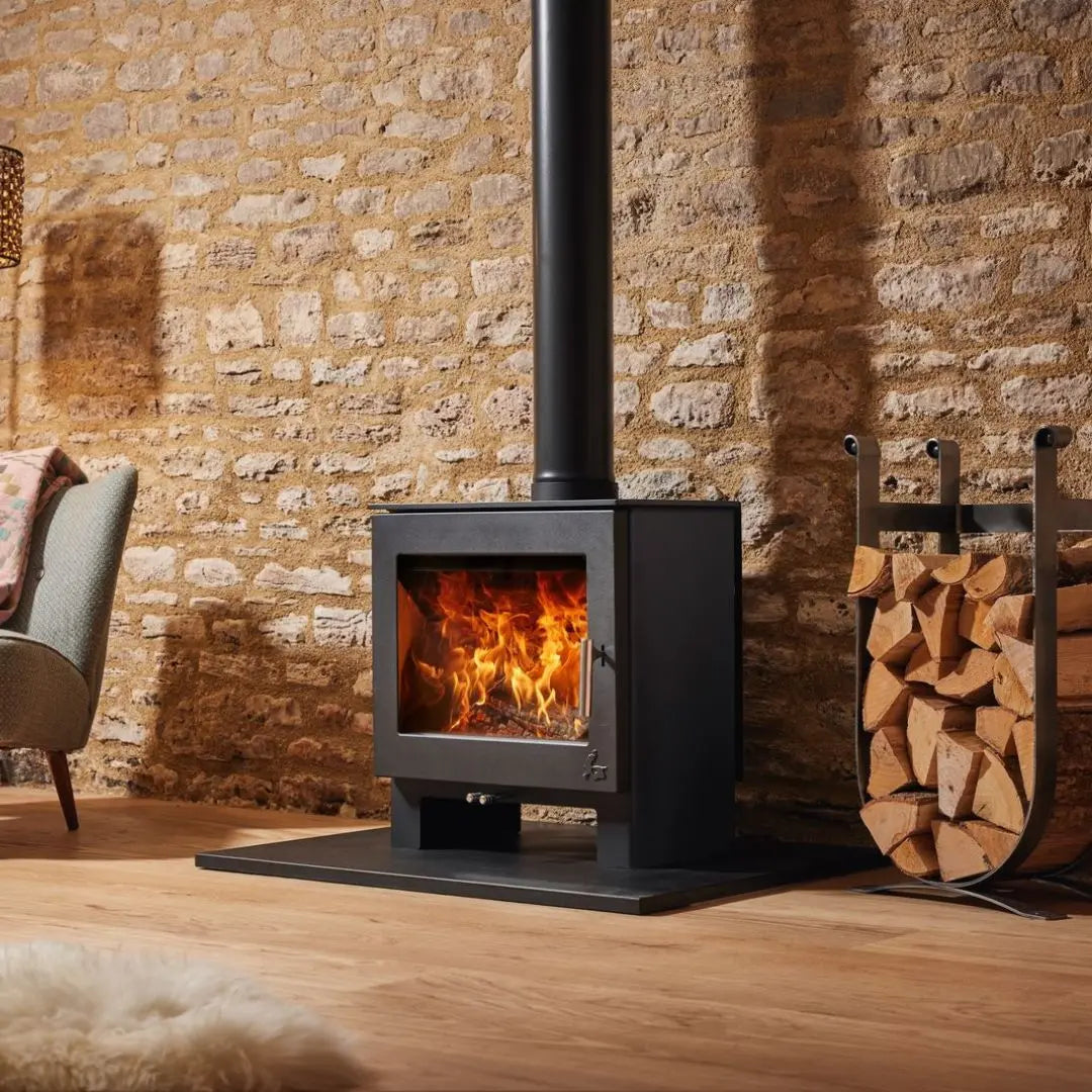 Dean Forge Sherford 8 Eco Stove - 8kW on black hearth against stone wall with log holder