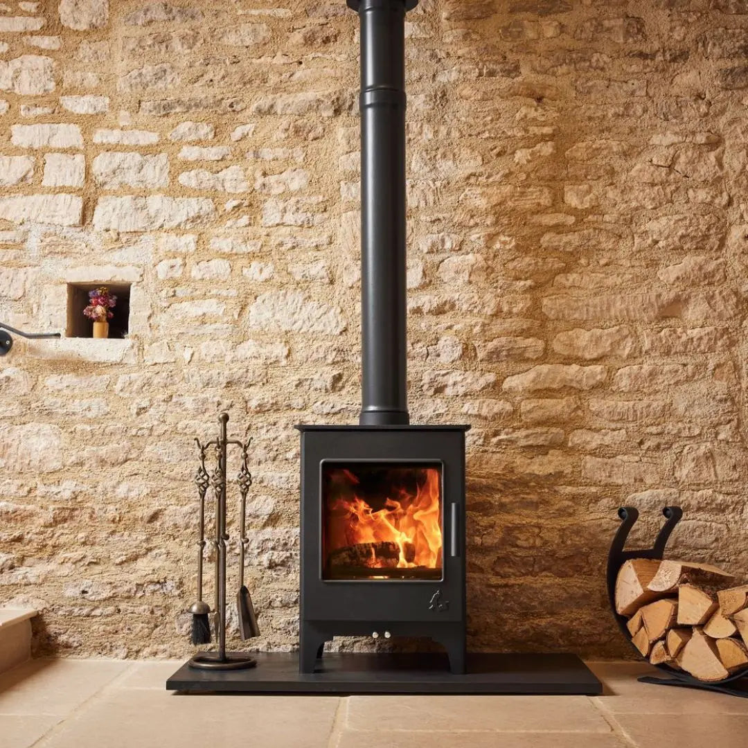 Dean Forge Woodbury 5 Eco Stove - 5kW on black hearth against stone wall with log holder
