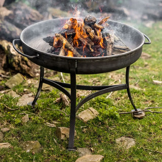 Dean Forge Firebowl Fire pit with burning logs on a grassy outdoor area