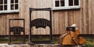 Three cast iron firewood holders on a log with a wooden building in the background