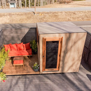 Modern outdoor sauna with red cushions and a wooden door on a deck.