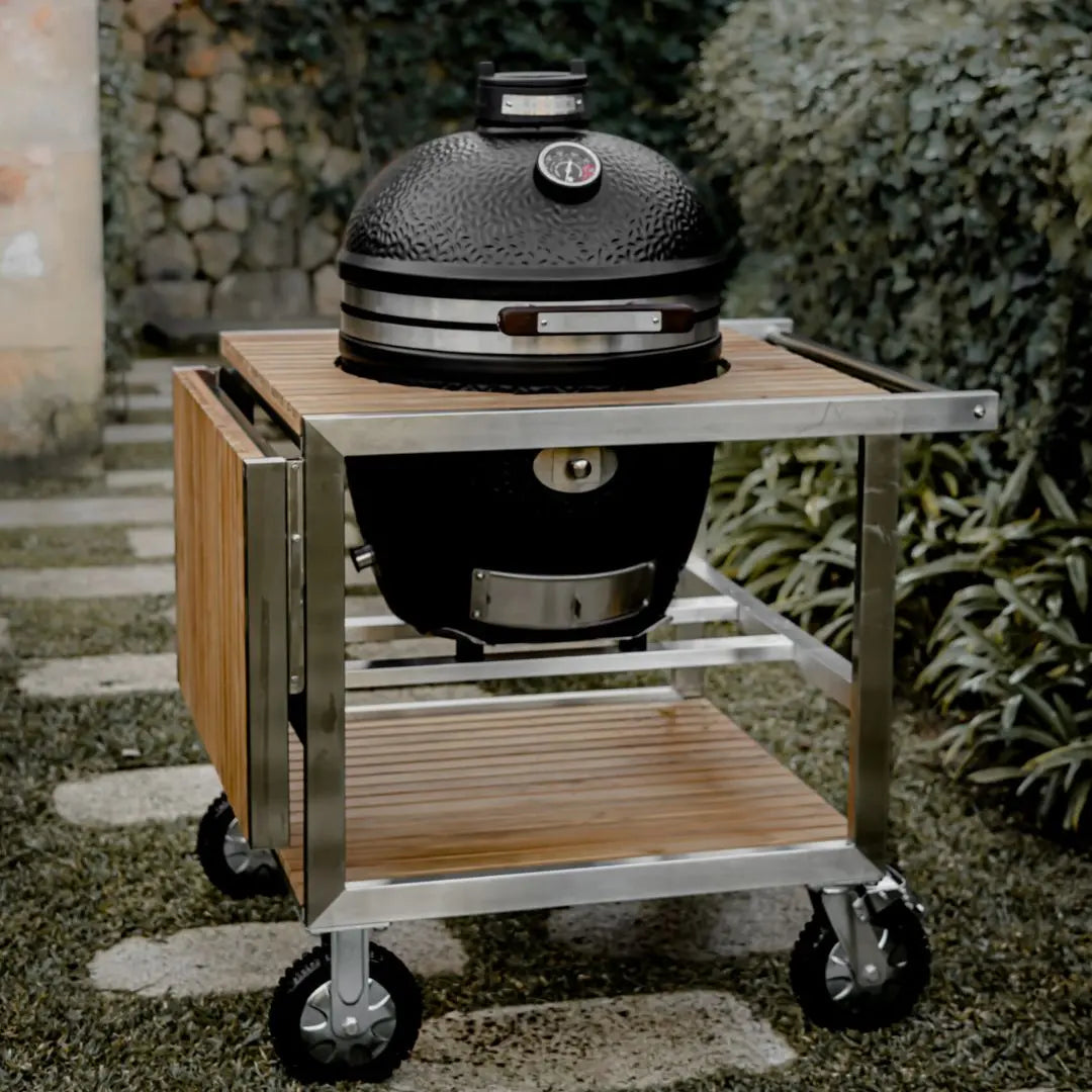 Black Monolith Avantgarde kamado grill with wooden cart table with a garden background