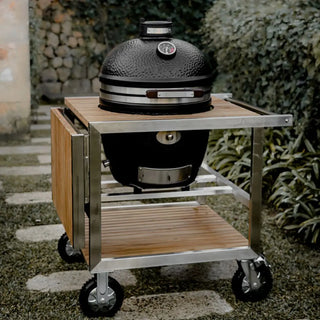 Black Monolith Avantgarde kamado grill with wooden cart table with a garden background