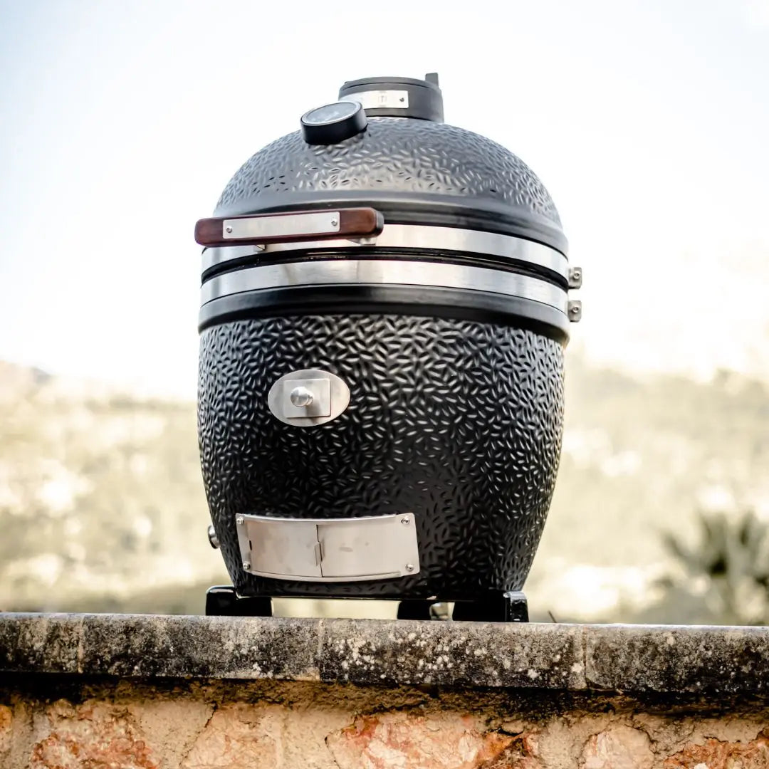Black textured Monolith Avantgarde kamado grill bbq on a stone ledge with a blurred natural background