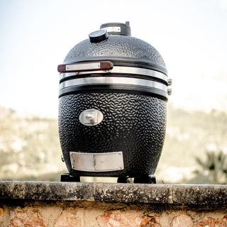 Black textured Monolith Avantgarde kamado grill bbq on a stone ledge with a blurred natural background