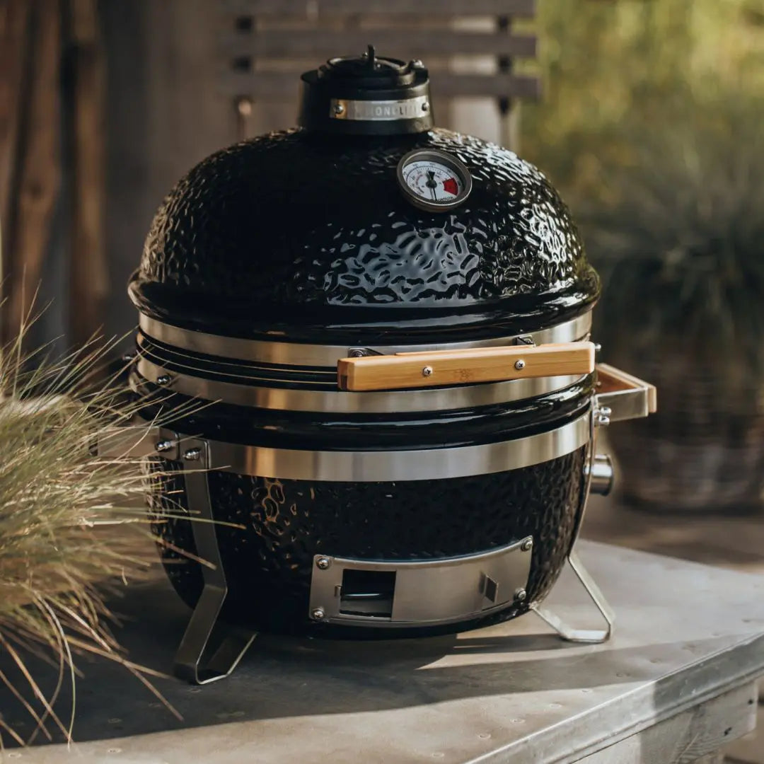 Monolith ICON 53cm Black Kamado-style grill on a stone surface with plants in the background