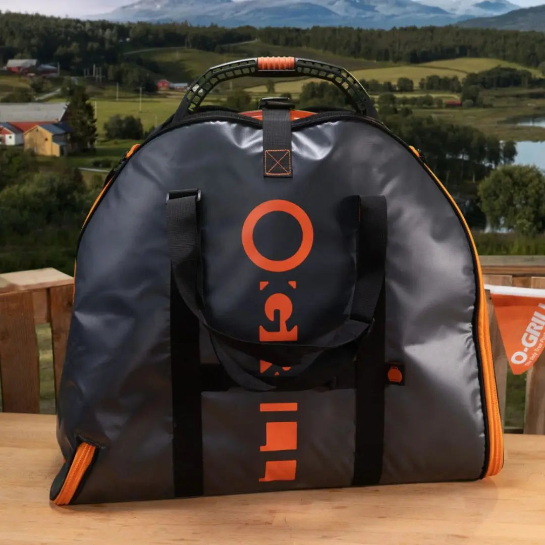 Black and orange bag with O-Grill logo for portable gas bbq grill on a wooden surface with a scenic background