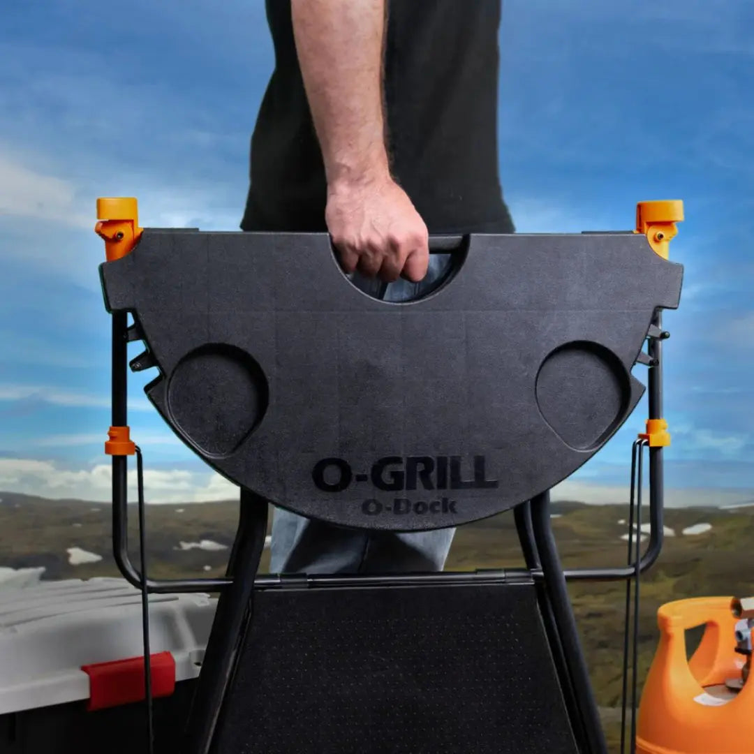 Person holding a black O-Grill with a scenic background