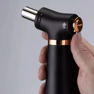 Black and rose gold handheld torch lighter held by a hand against a grey background