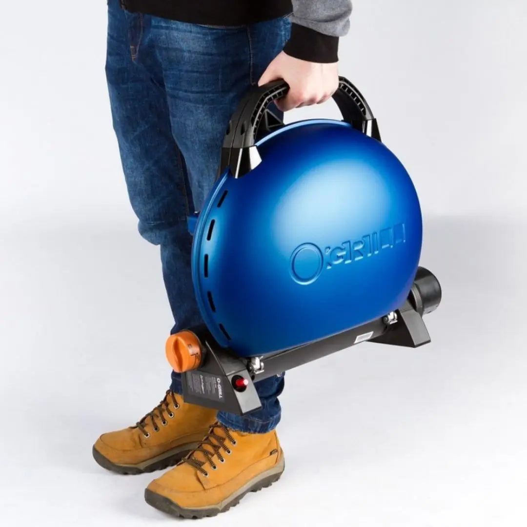 Person holding a blue O-Grill portable gas grill bbq with brand logo on a white background
