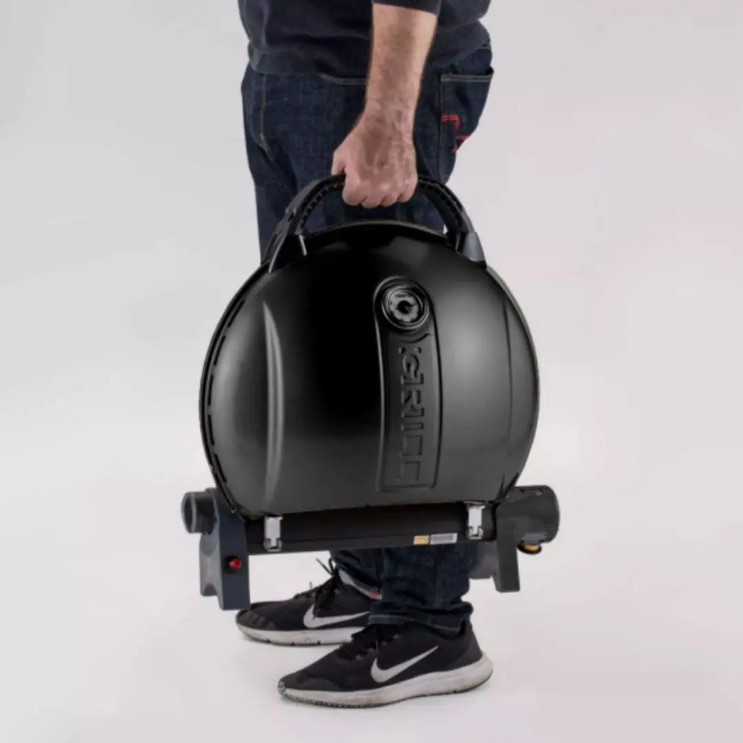 Person holding a black portable O-Grill gas bbq grill on a white background
