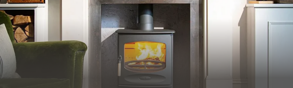 A lit wood-burning stove in a living room fireplace, with an armchair beside it